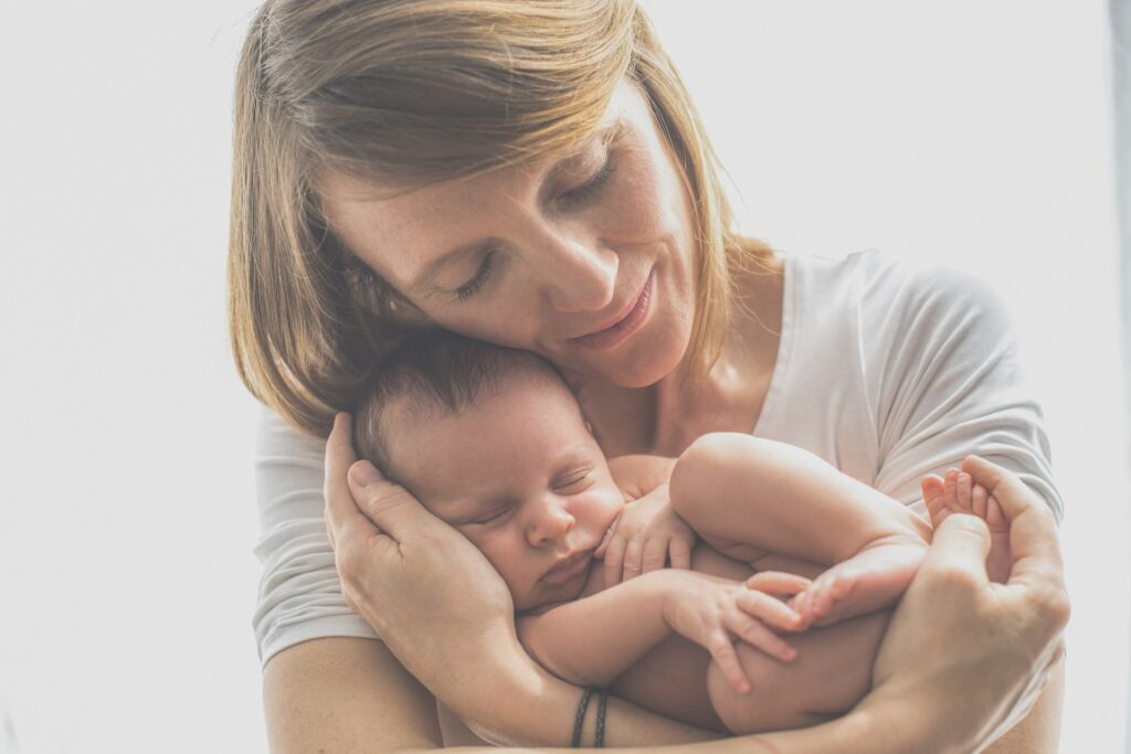 Les yeux fermés, une mère sourit et prend dans ses bras son bébé qui dort paisiblement en position foetale