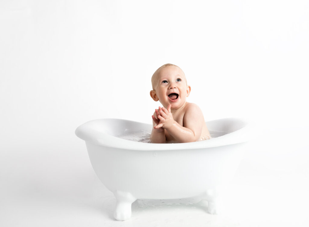 Un bébé, dans un décor complètement blanc, sourit et tape des mains ans son bain. C'est une baignoire d'un blanc éclatant et avec des pieds en finition royale.