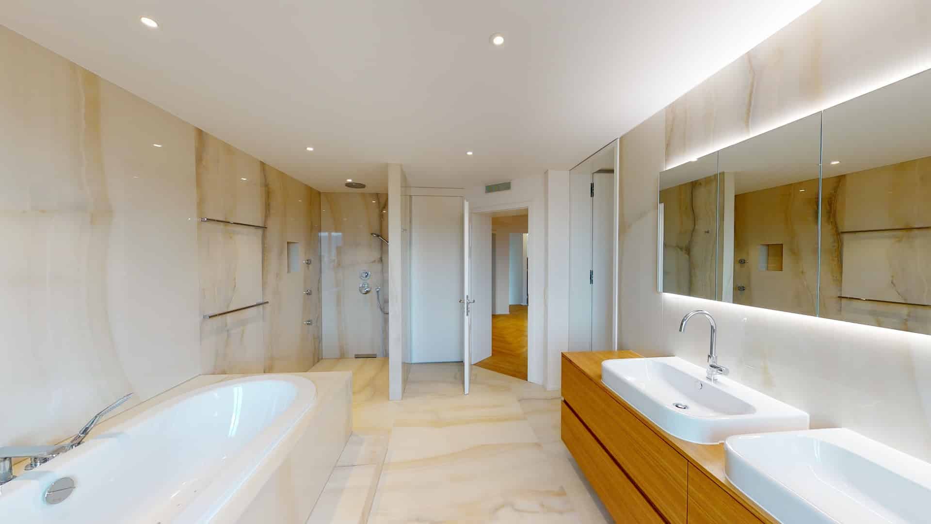 Salle de bain avec baignoire. Il y a deux lavabos sur le côté avec un grand miroir et des leds qui illuminent la pièce.