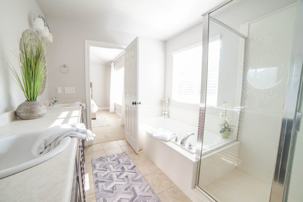 Un salle de bain blanche avec une baignoire qui s'appuie sur l'espace douche. Il y a un lavabo avec un tapis à terre.