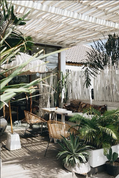 Balcon avec plafond et mur en pailles. Salon de jardin en rotin beige avec plantes autour.
