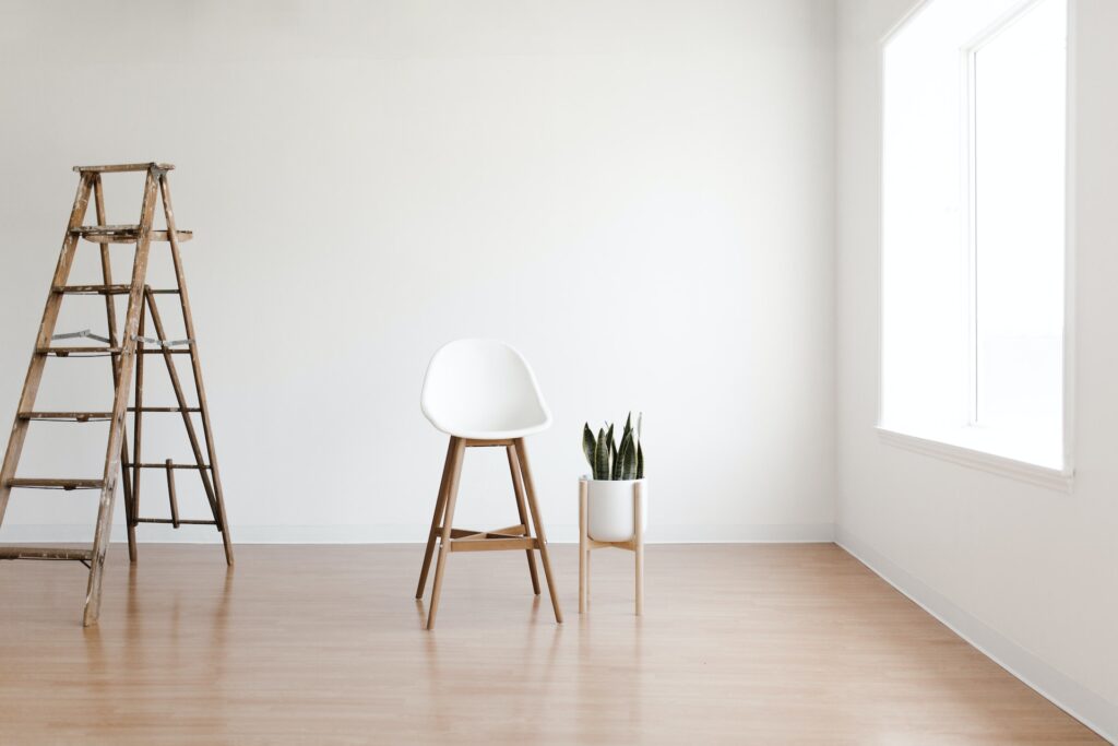 pièce minimaliste avec peu d'éléments, on voit une chaise blanche, une échelle et une plante