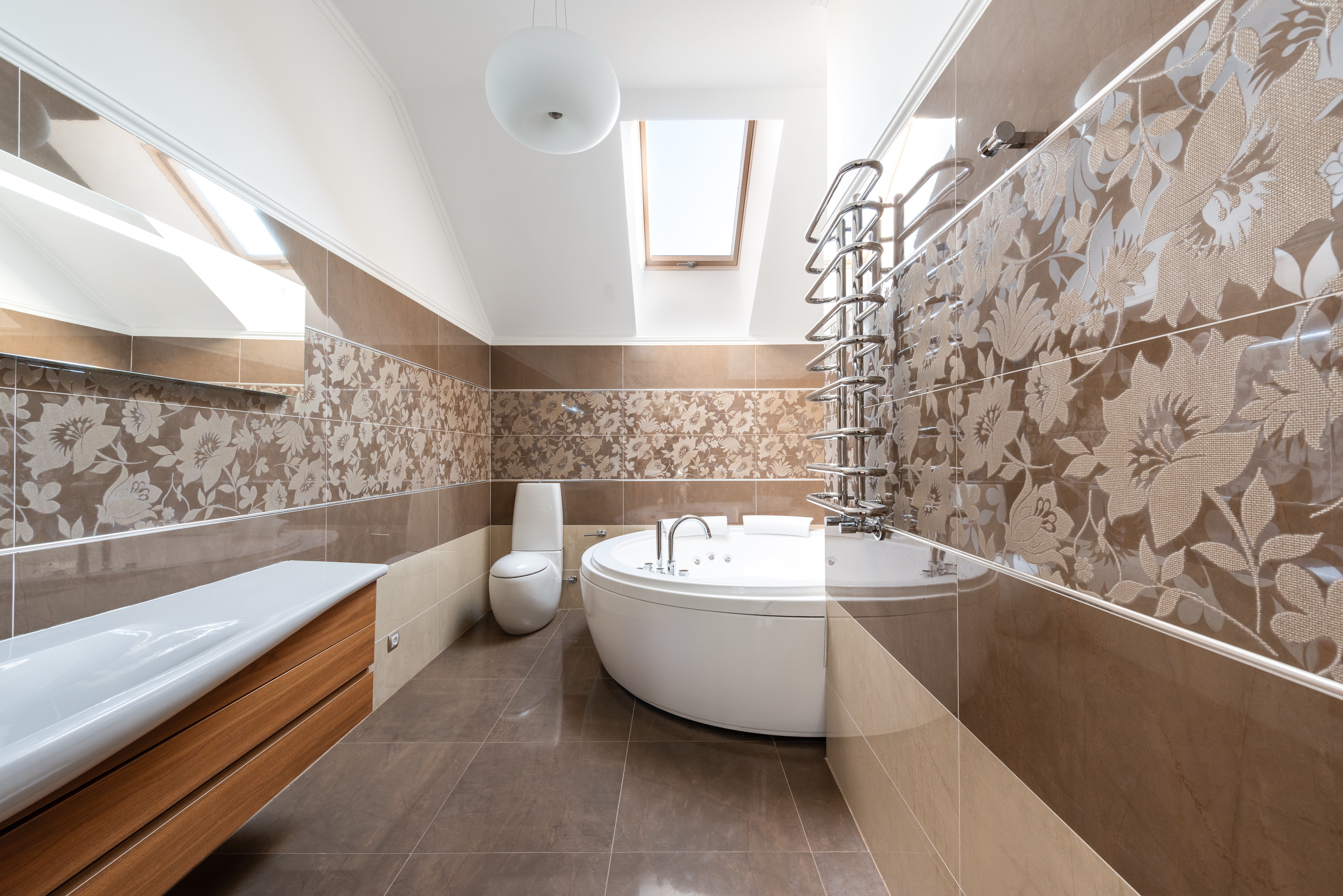 Salle de bain avec carrelage mural à motifs marron clair. La baignoire est grande et blanche, le lavabo est blanc et marron clair.