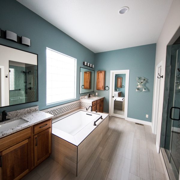 Salle de bain rectangulaire. Les murs sont bleu, le carrelage est en aspect parquet gris. Les meubles sont en bois marron.